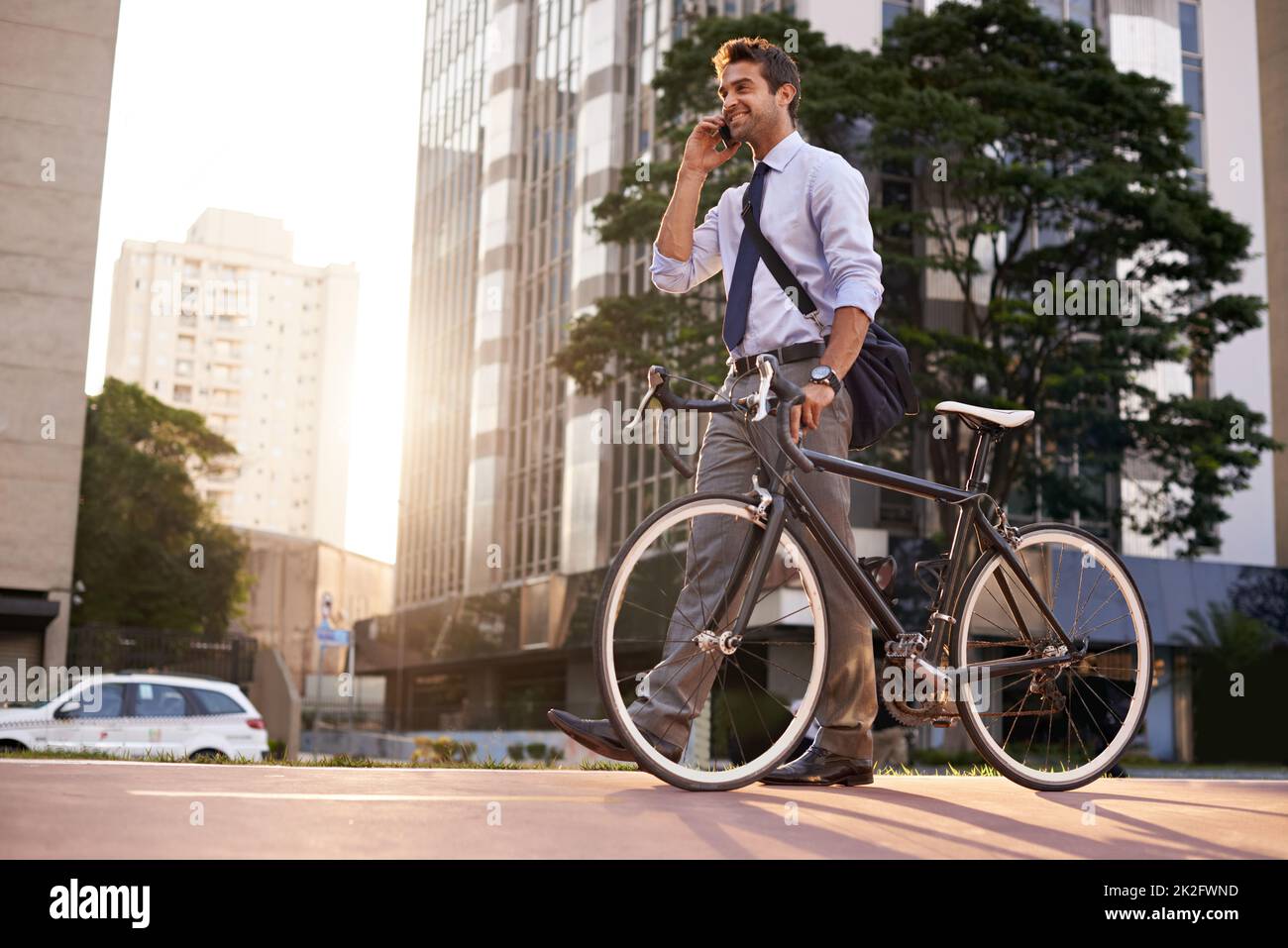 Business on the go. Shot of a businessman taking a phone call while commuting to work with his bicycle. Stock Photo