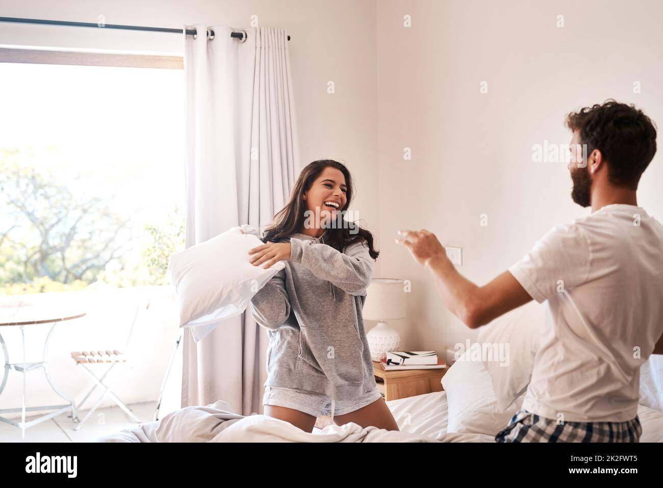 Start every morning with silliness. Shot of a happy young couple having a pillow fight in bed. Stock Photo