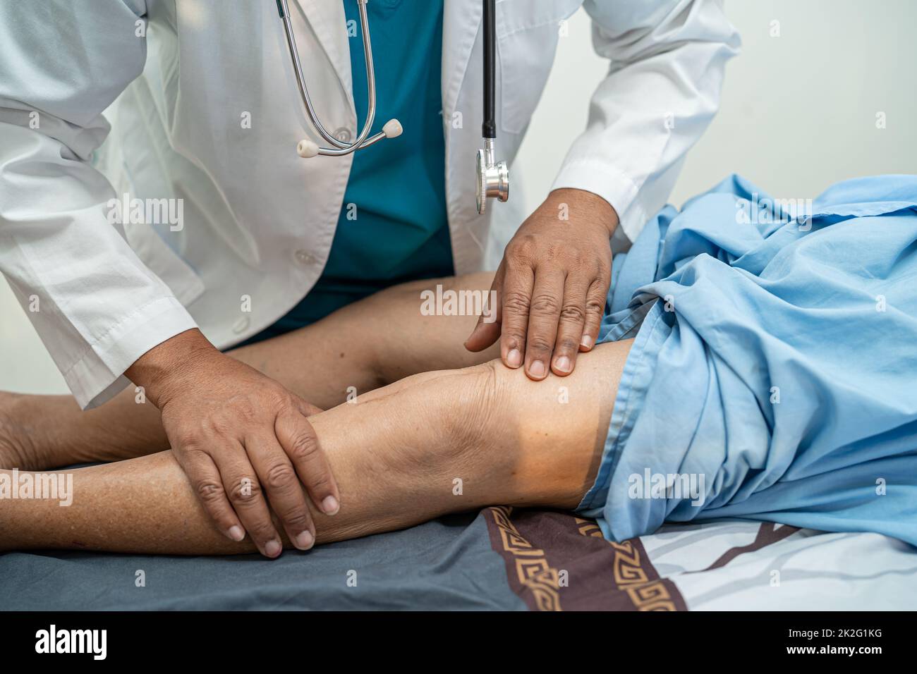 Asian doctor physiotherapist examining, massaging and treatment knee and leg of senior patient in orthopedist medical clinic nurse hospital. Stock Photo