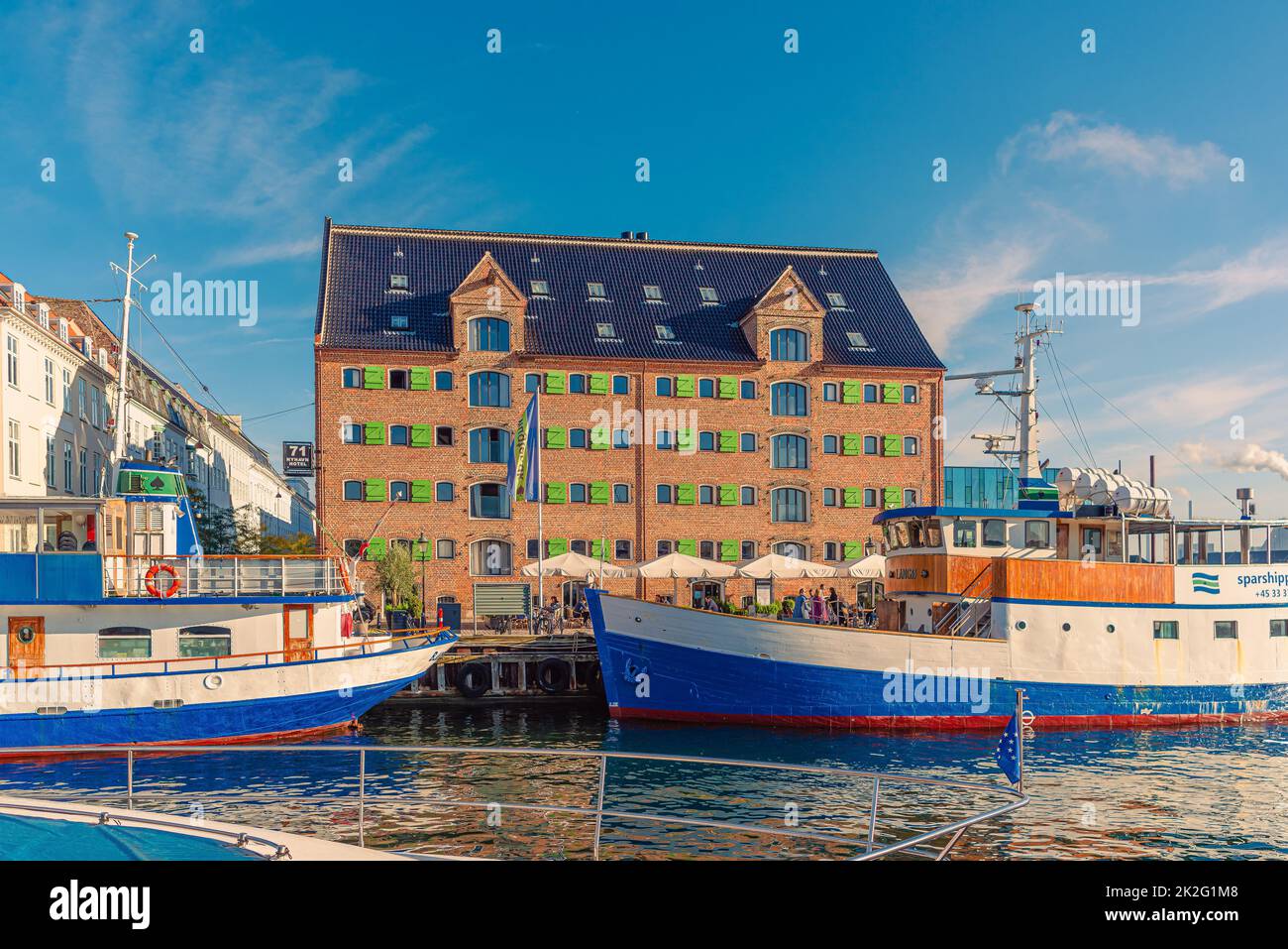 71 Nyhavn Hotel, on the Nyhavn canal, which is located in a old brick warehouse building and several ships in front of it. Copenhagen, Denmark Stock Photo