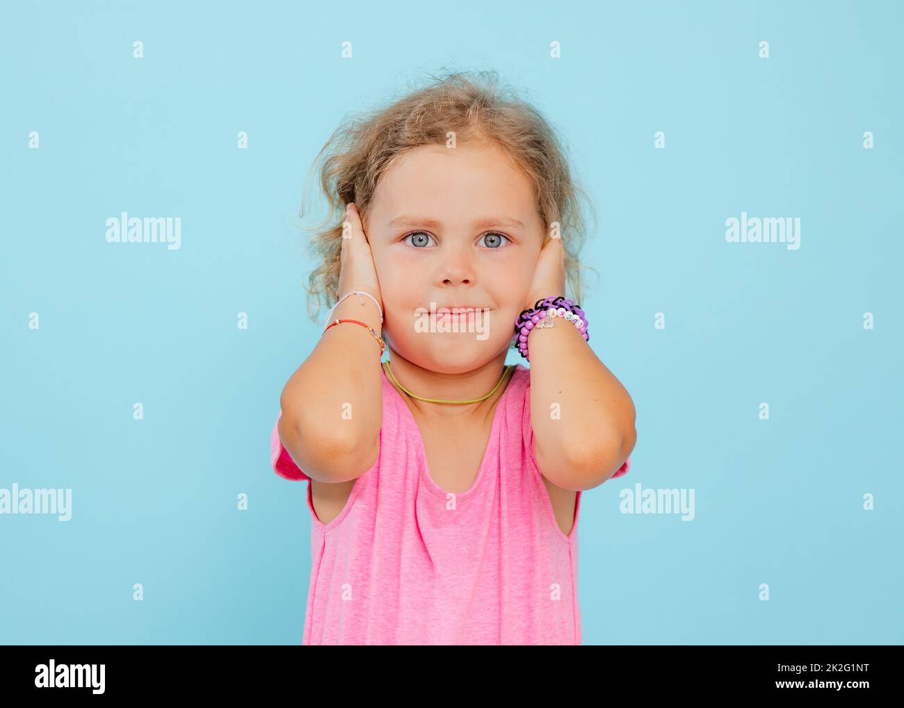 Charming little girl cover ears with hands on empty blue background