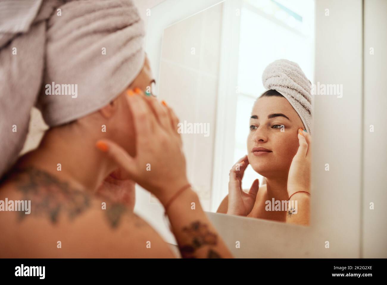 What you do is a reflection of you. Shot of an attractive young woman inspecting her face in the bathroom mirror. Stock Photo