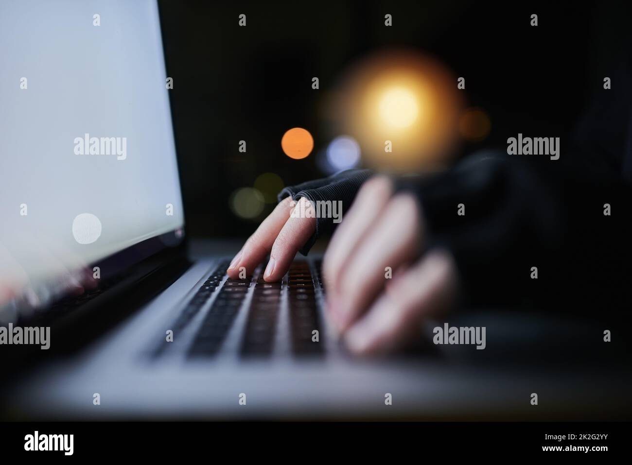 Be careful what you share online. Shot of an unrecognizable computer hacker using a laptop late at night. Stock Photo