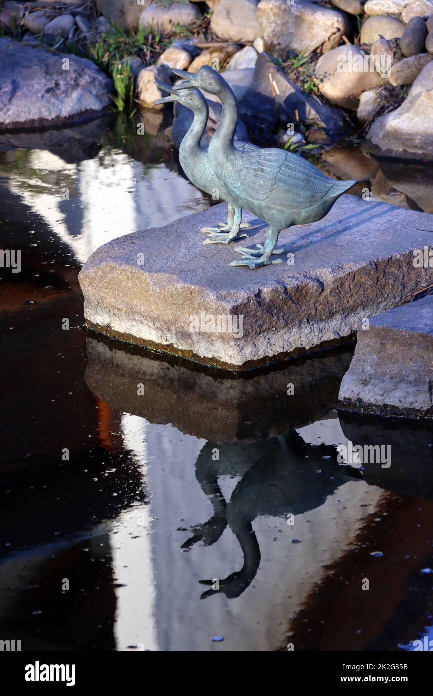zwei dekorative Enten aus Metall spiegeln sich im Gartenteich Stock Photo