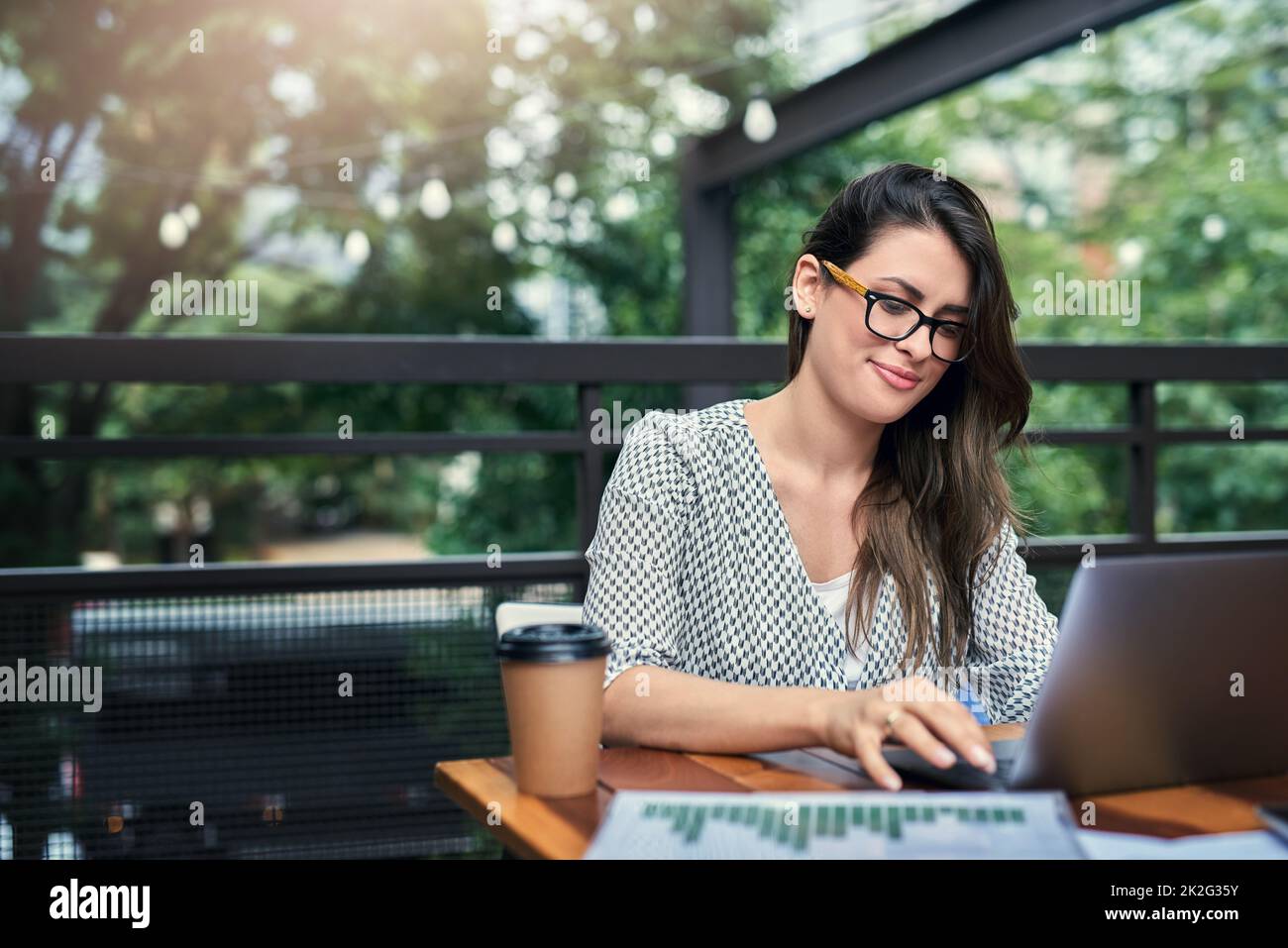Being productive outside of the office. Cropped shot of an attractive young businesswoman working on her laptop while sitting outdoors at a cafe. Stock Photo