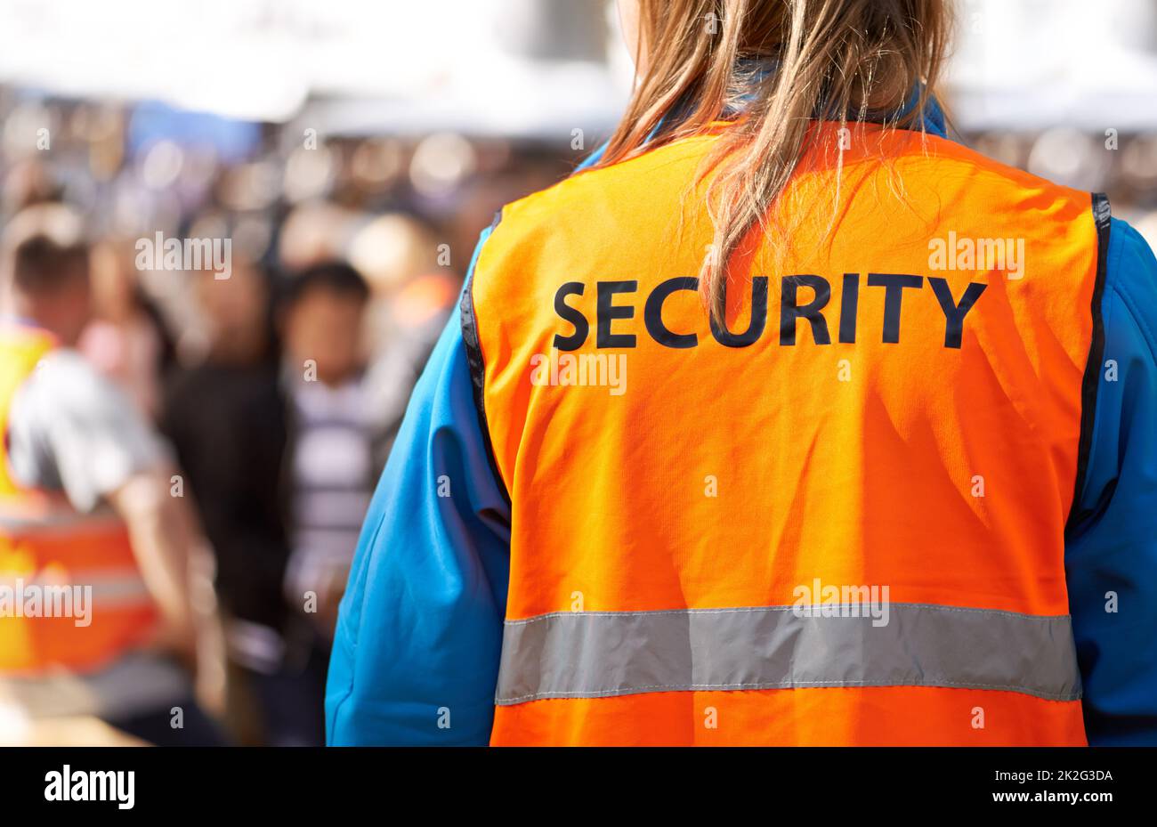 Safety is the main aim. Rearview shot of a security officer standing outdoors with a crowd in the background. Stock Photo
