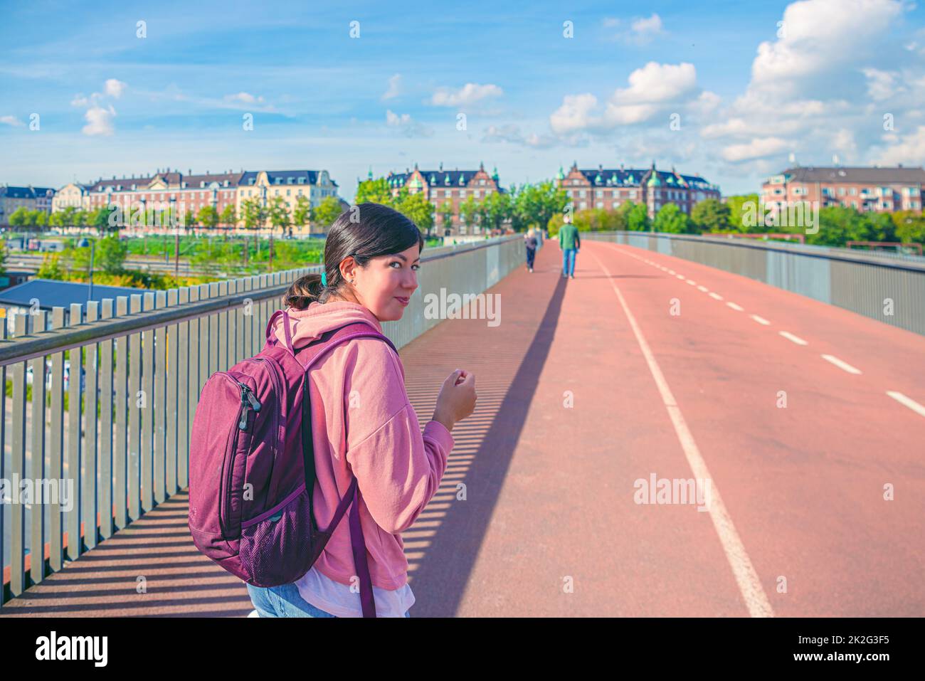 Smiling student brunette girl walking along pedestrian and bicycle bridge  across the railway  to the residential buildings. Copenhagen, Denmark Stock Photo