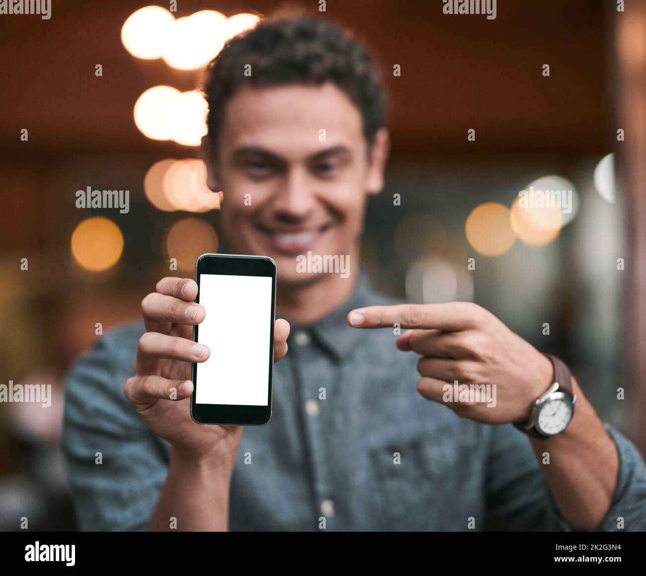 Looks like were getting popular. Shot of a confident young man holding up a cellphone to the camera while standing inside of a beer brewery during the day. Stock Photo