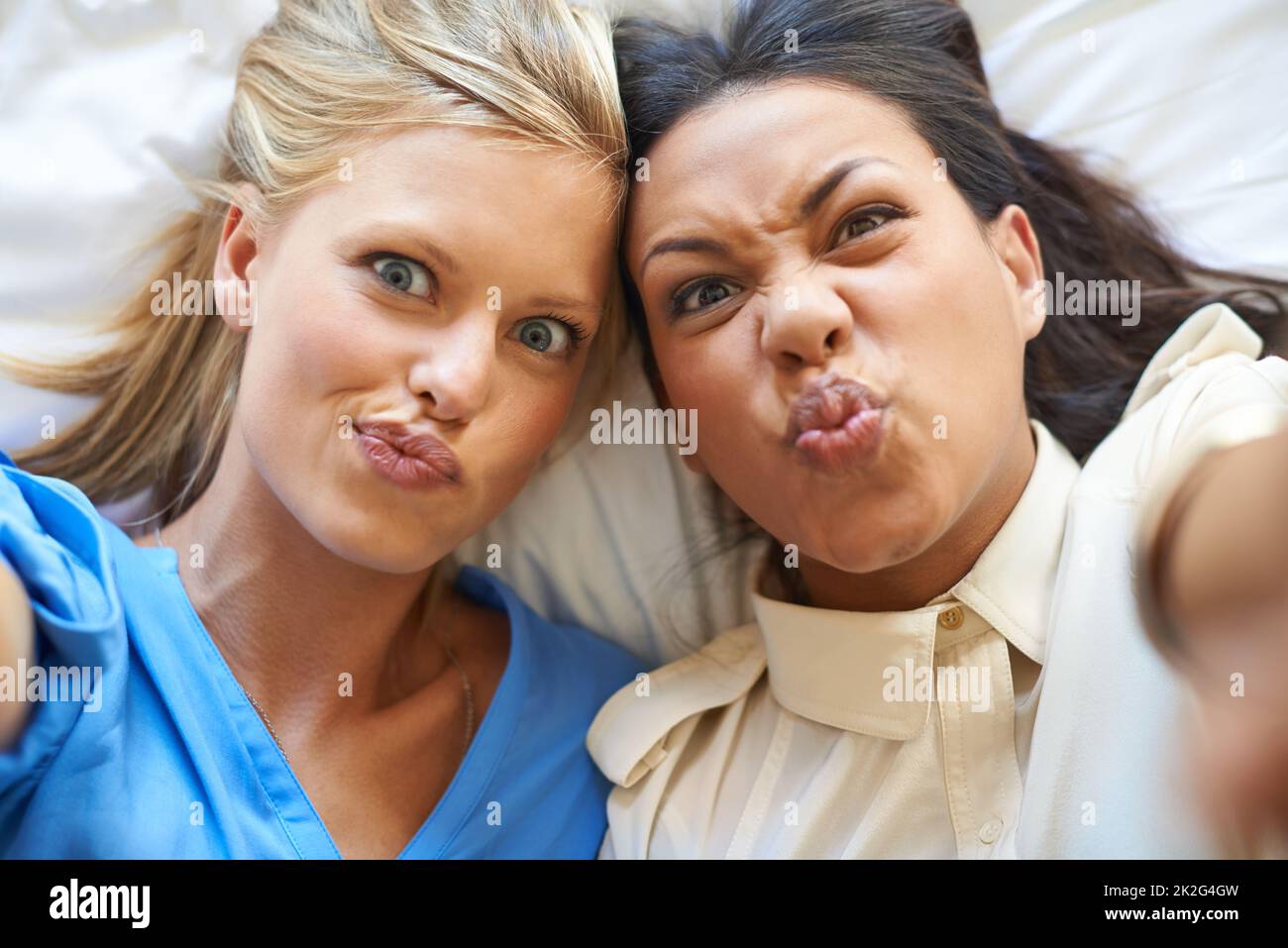 Make a face. High angle portrait of two attractive young women taking selfies while lying on a bed. Stock Photo