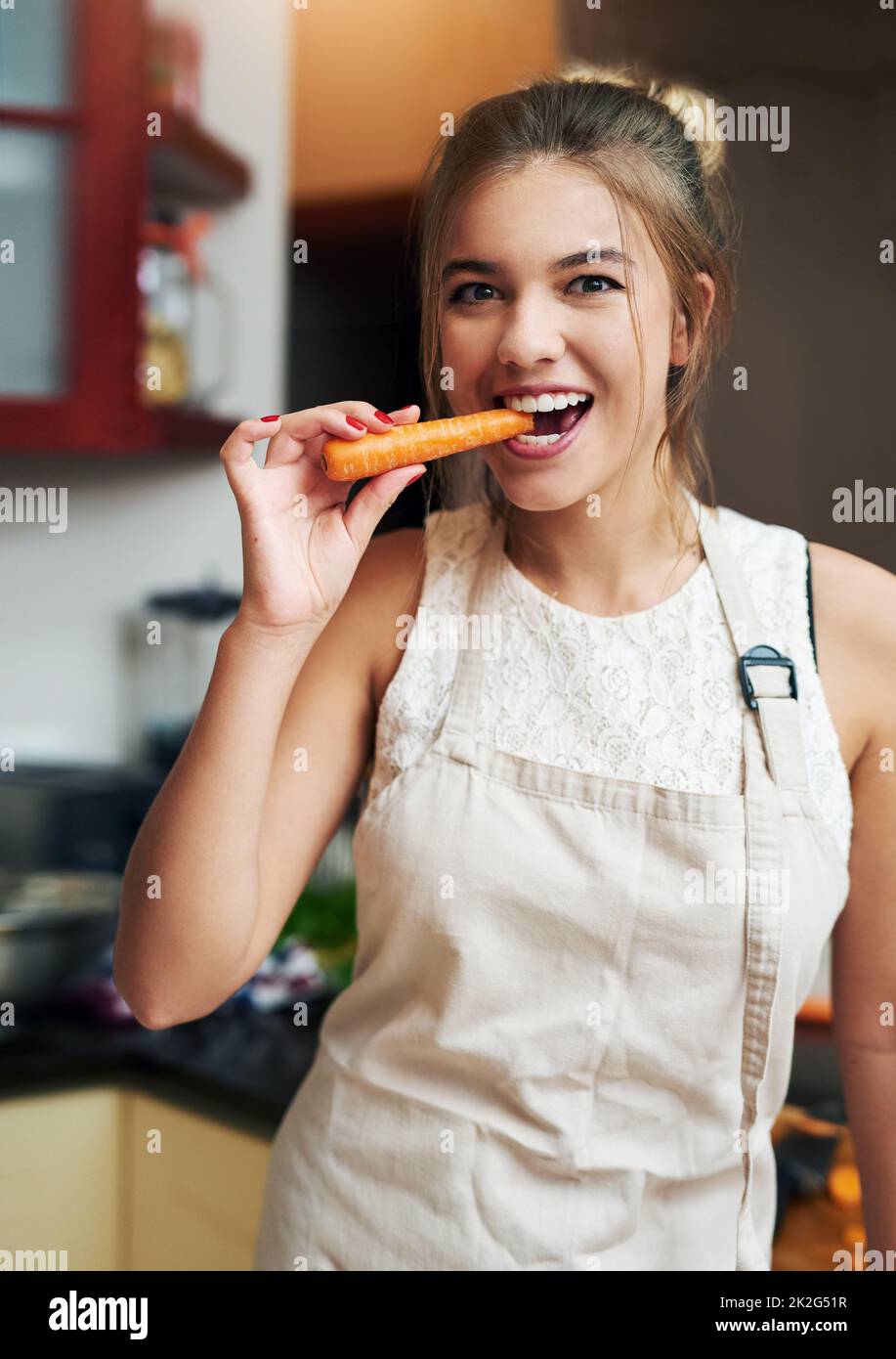 When hunger strikes.... Cropped portrait of an attractive young woman taking a bite of a carrot at home. Stock Photo