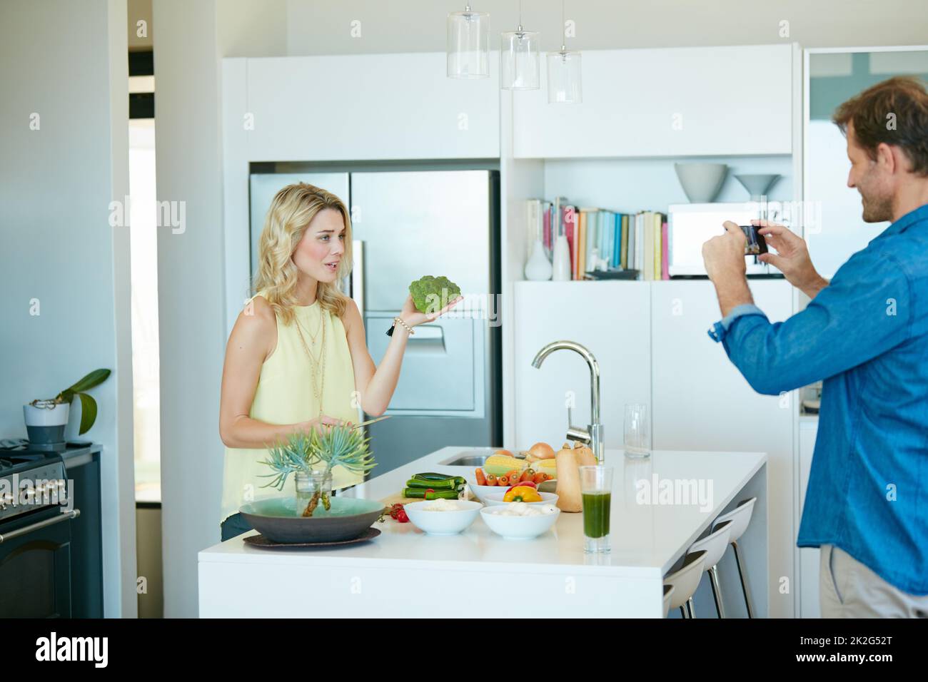 The star of the show is broccoli. Shot of a husband taking snapshots of his wife preparing a healthy meal at home. Stock Photo