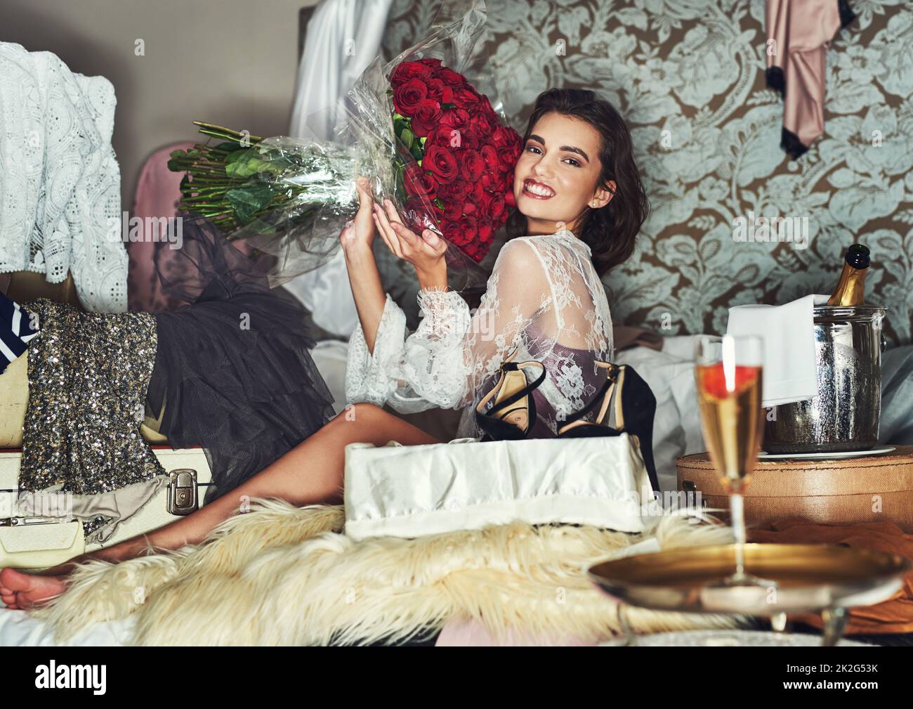 Flowers always puts me in a good mood. Portrait of a beautiful young woman relaxing on her bed and being surrounded by gifts while holding a bouquet of roses. Stock Photo