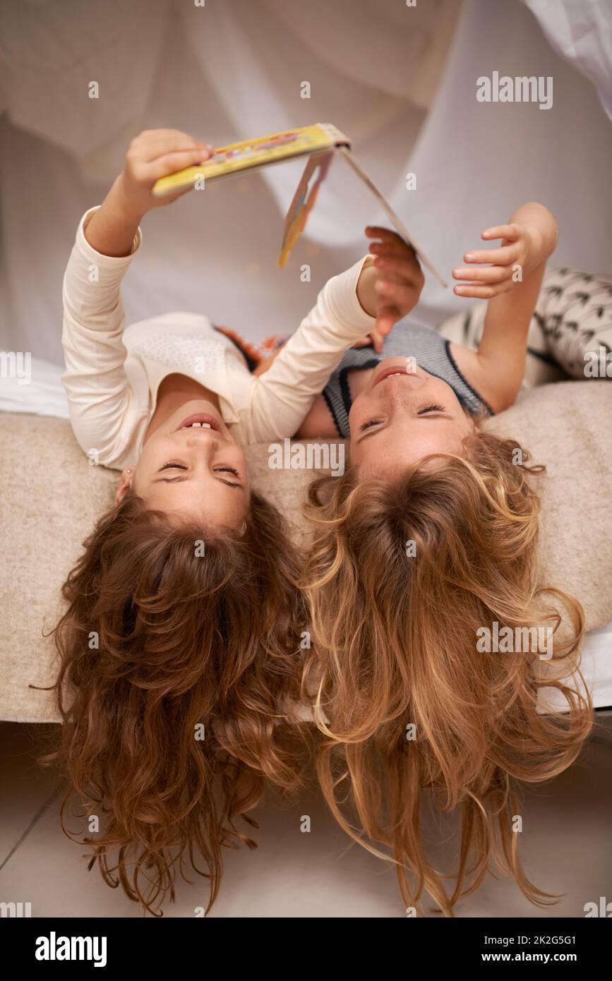 Turning the story on its head. Shot of two little girls reading a book while lying upside down on a bed. Stock Photo
