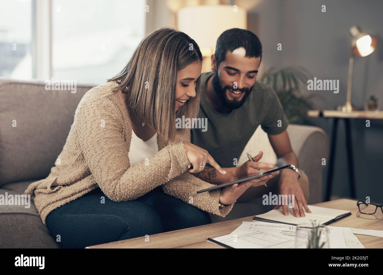 Improving their finances one tap at a time. Shot of a young couple sing a digital tablet while going through paperwork at home. Stock Photo