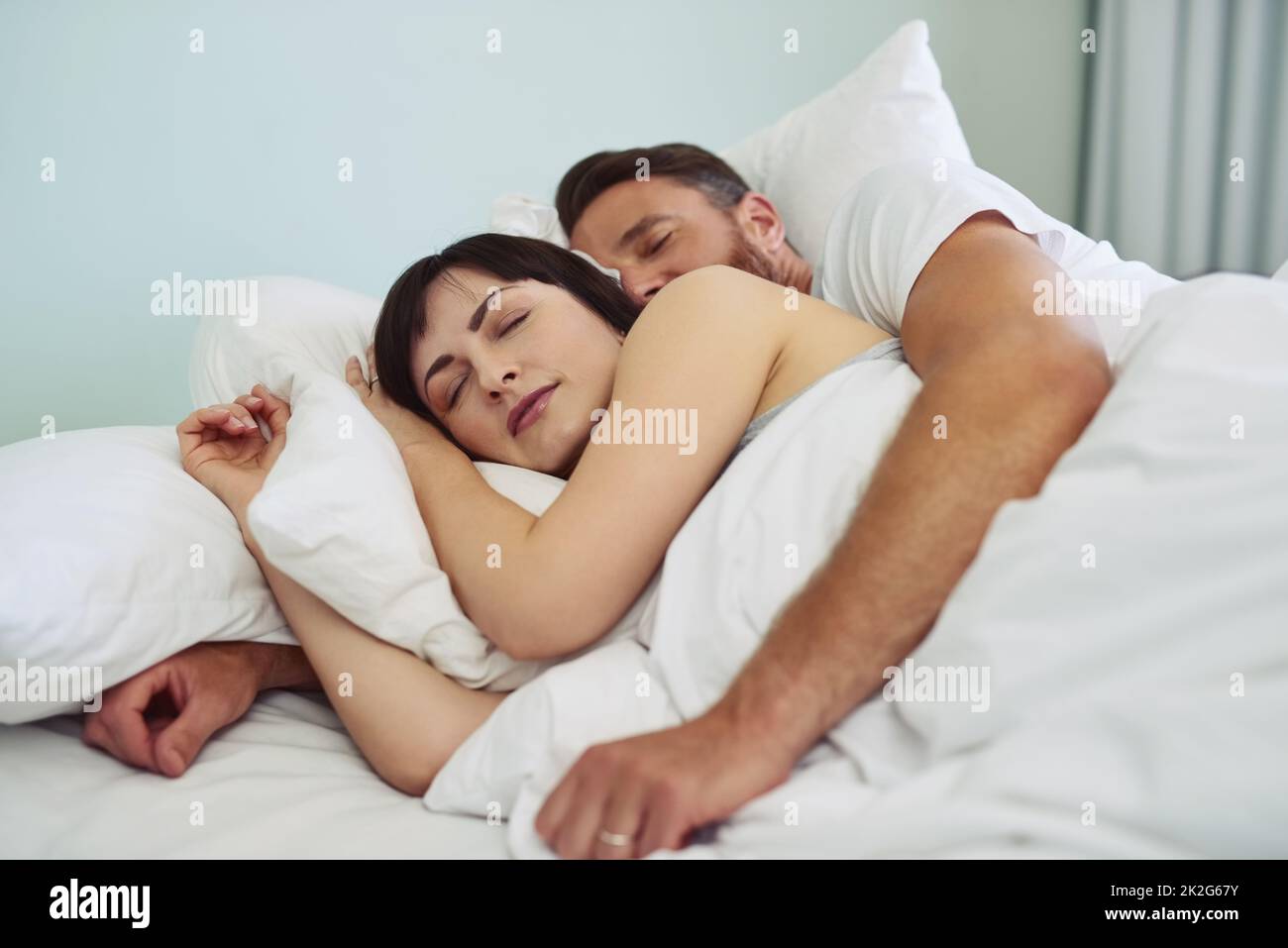 Too comfortable to get out of bed. Shot of a relaxed young couple sleeping in each others arms in bed during morning hours. Stock Photo