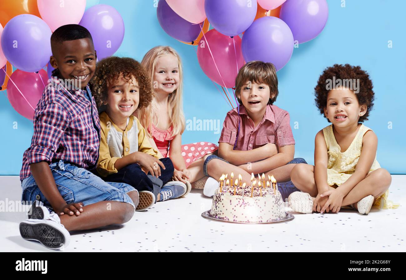 My birthday wish is to be friends forever. Shot of a group of children sitting around a birthday cake with bunch of balloons in the background. Stock Photo