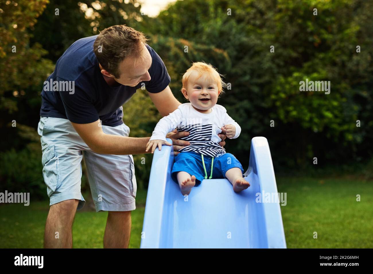 Daddys helping me slide. Shot of an adorable little boy and his father playing in the backyard. Stock Photo