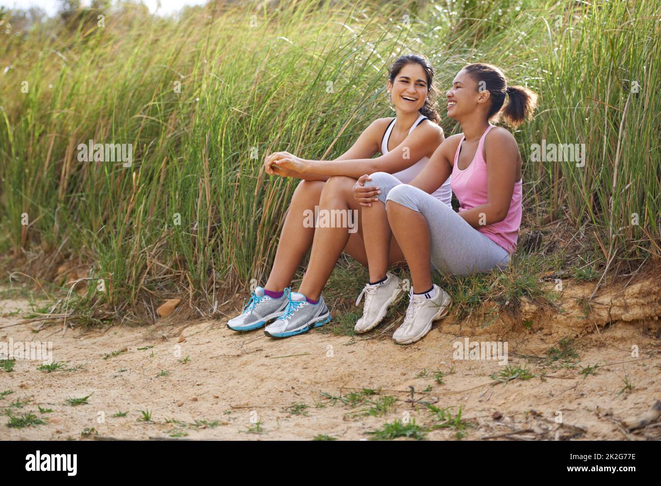 Sharing a joke between friends. Two friends sitting outside laughing together while wearing exercise clothes. Stock Photo
