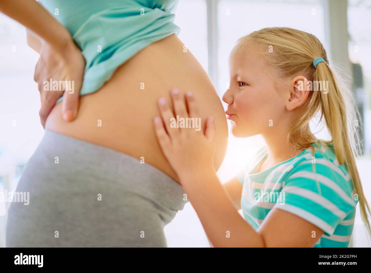 Were going to have so much fun, little baby. Shot of a little girl kissing her mothers pregnant belly at home. Stock Photo