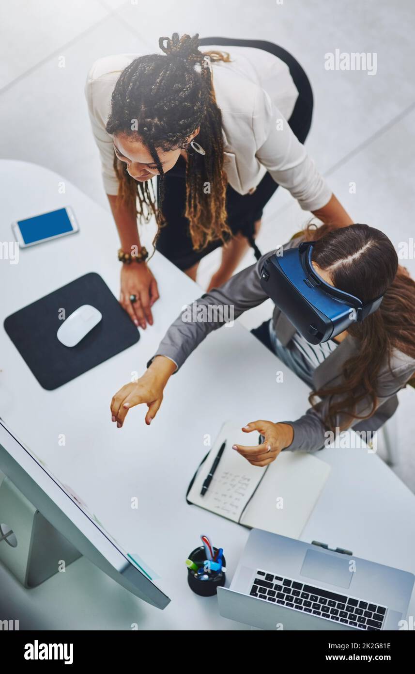 High angle shot of a young businesswoman using a VR headset while being assisted by a female colleague. Stock Photo