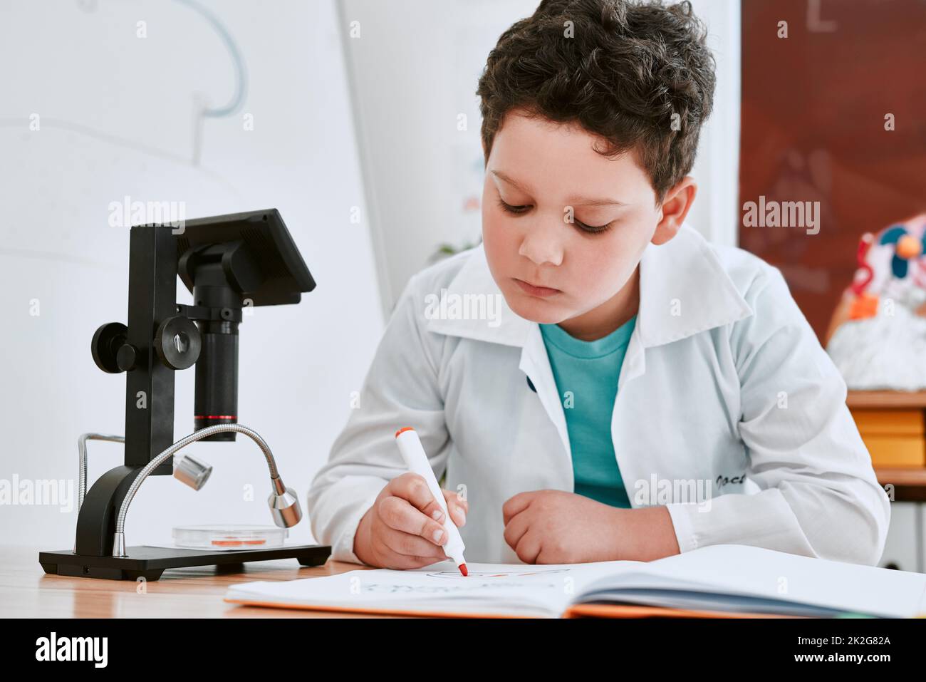 Getting top grades is what he always strives for. Shot of an adorable young school boy writing notes in his note book in science class at school. Stock Photo