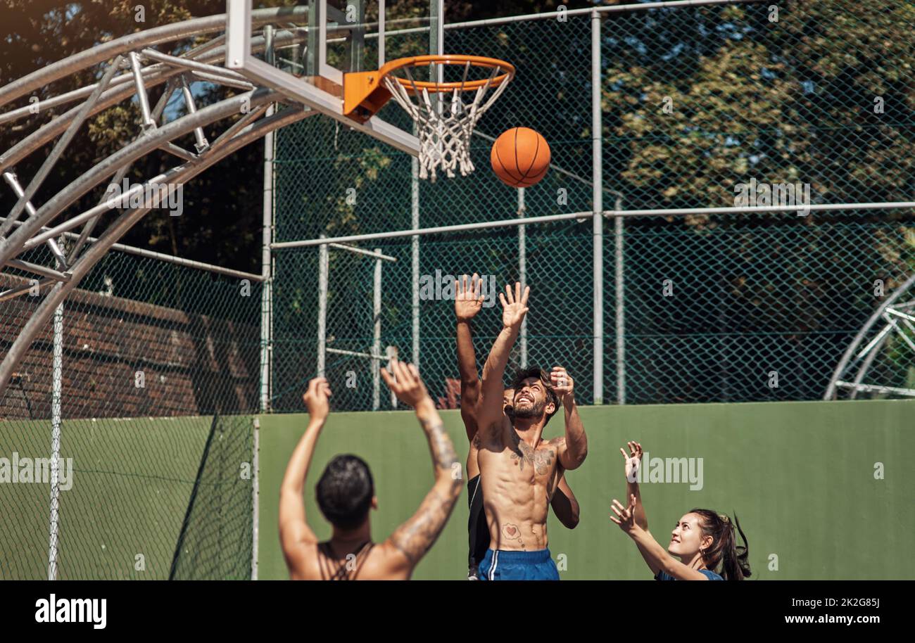 Will he make the shot. Shot of a group of sporty young people playing basketball on a sports court. Stock Photo