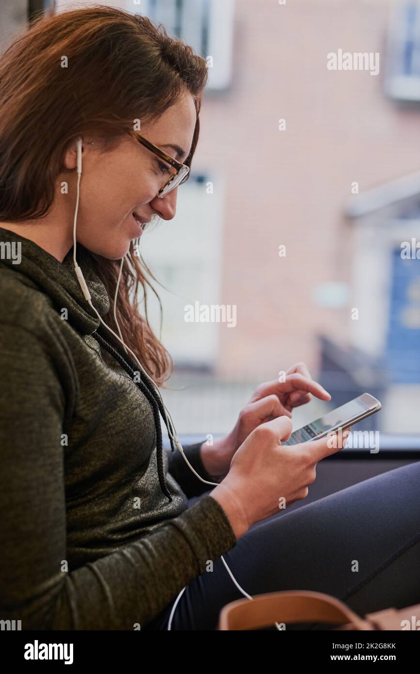 Checking the bus routes online. Cropped shot of an attractive young woman listening to music while sitting on a bus. Stock Photo