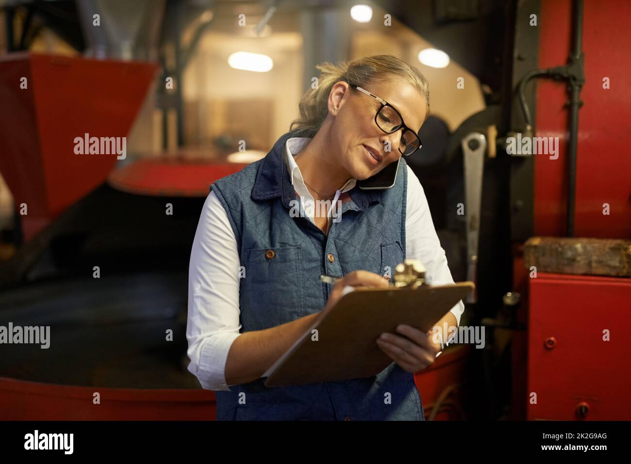 Multitasking like a pro. Shot of an industrious entrepreneur answering her phone while working in her roastery. Stock Photo
