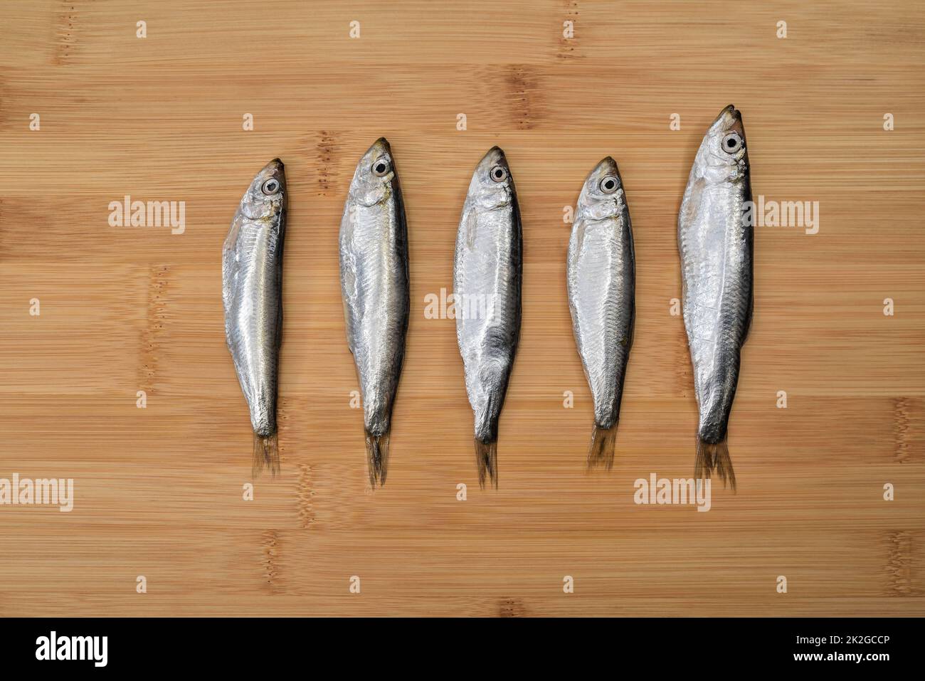 Top view of fresh anchovies on wooden cutting board background. Raw fish prepared for cooking. Stock Photo