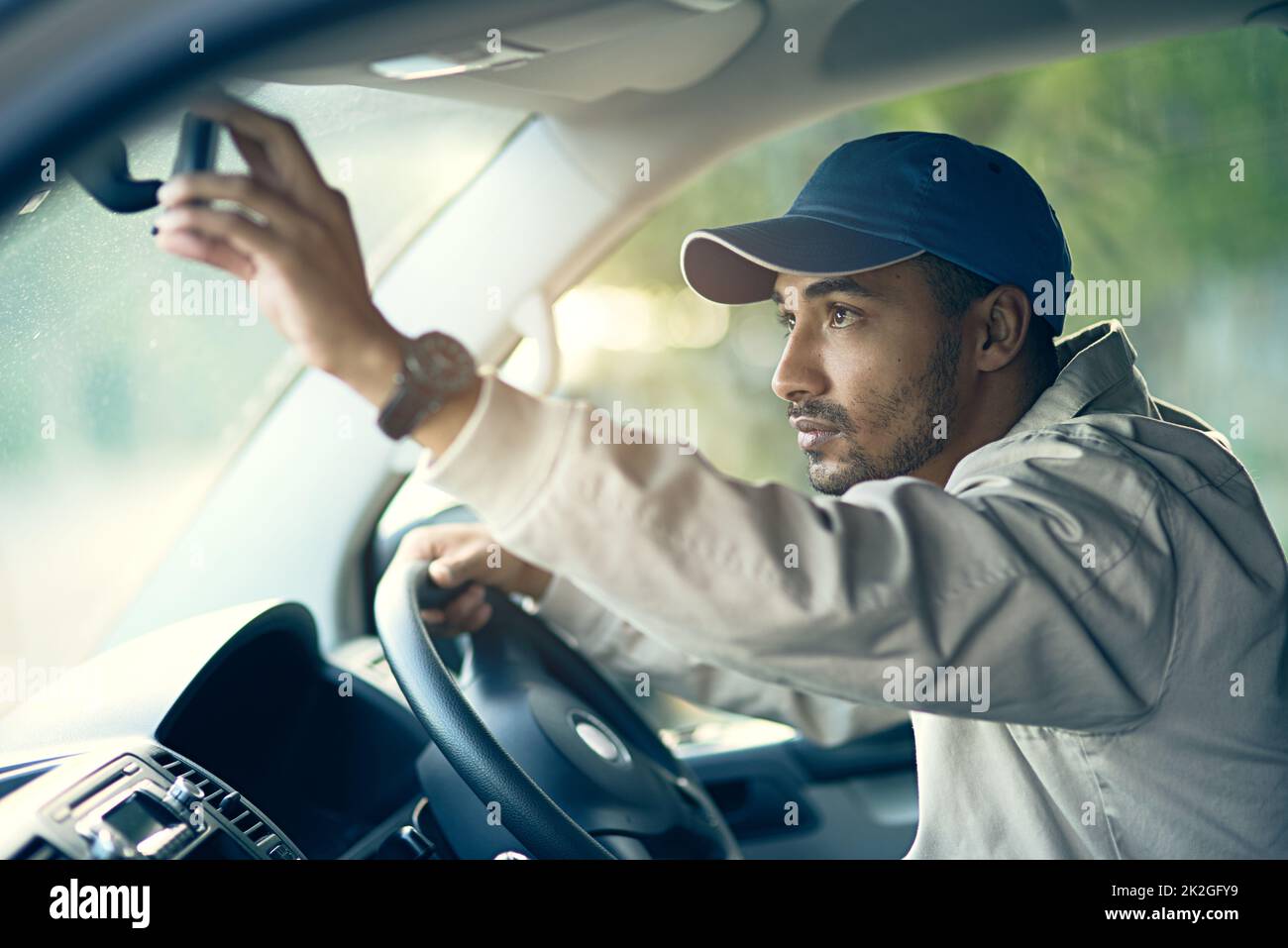 Off to make his next delivery stop. Cropped shot of a delivery man adjusting the rear-view mirror of his van. Stock Photo