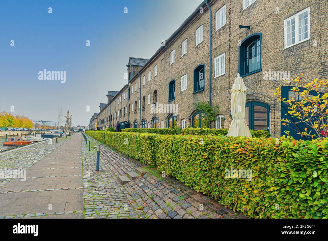 Many three-story buildings made of gray bricks on a street with a stone pavement near the river channel on the neighbourhood Christianshavn.Copenhagen, Denmark Stock Photo