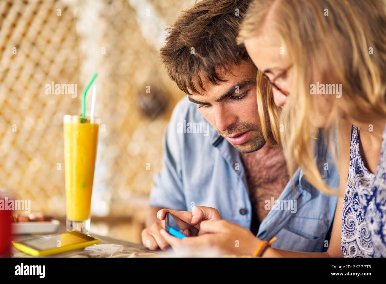 Let me see those coordinates again. Shot of a young couple looking at a cellphone together while relaxing in a restaurant. Stock Photo