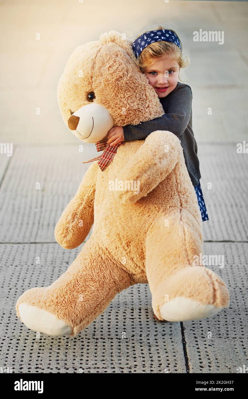 The bigger the bear, the bigger the cuddles. Portrait of a cute little girl holding an enormous teddybear while playing outside. Stock Photo