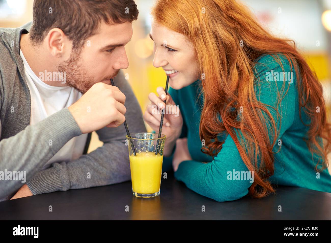 Juicy romance. Cropped shot of a happy young couple sharing a glass of juice on a date at a cafe. Stock Photo