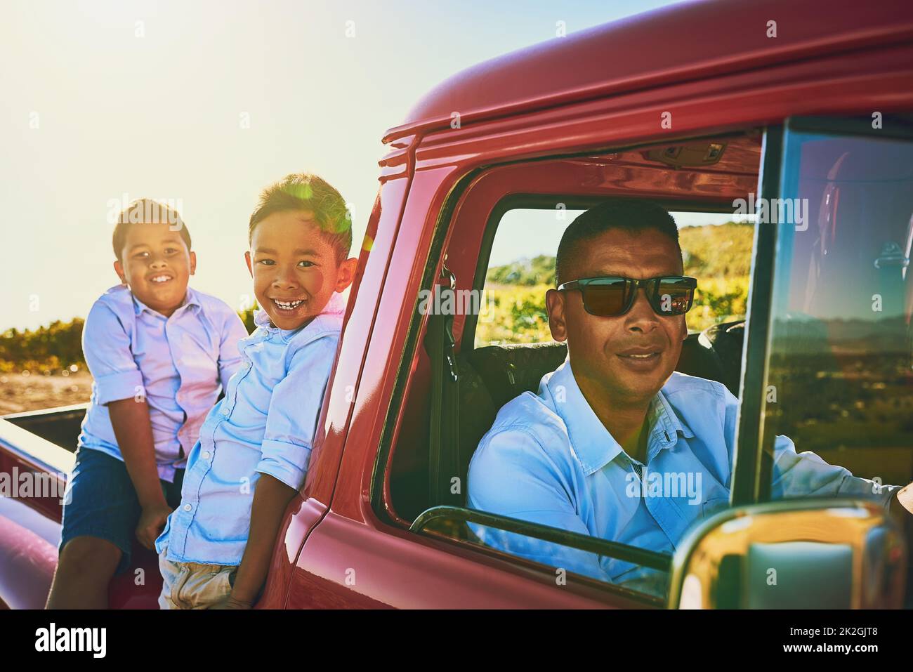 The boys are ready to take a drive. Shot of a cheerful father wearing sunglasses while sitting inside of a red pickup truck with his two young sons. Stock Photo
