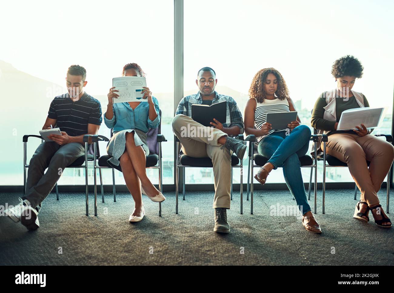 Shot of a group of young focussed work colleagues seated on chairs next to each other in a row while making notes inside of the office during the day Stock Photo