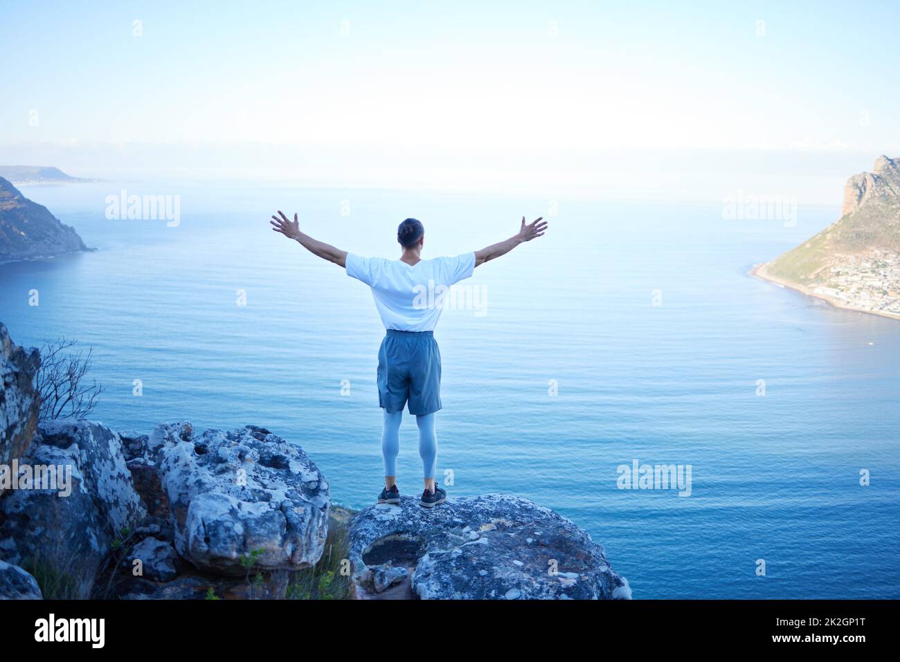 This is freedom. Rearview shot of an unrecognizable young man standing with his arms outstretched while looking at the ocean view from the mountain. Stock Photo