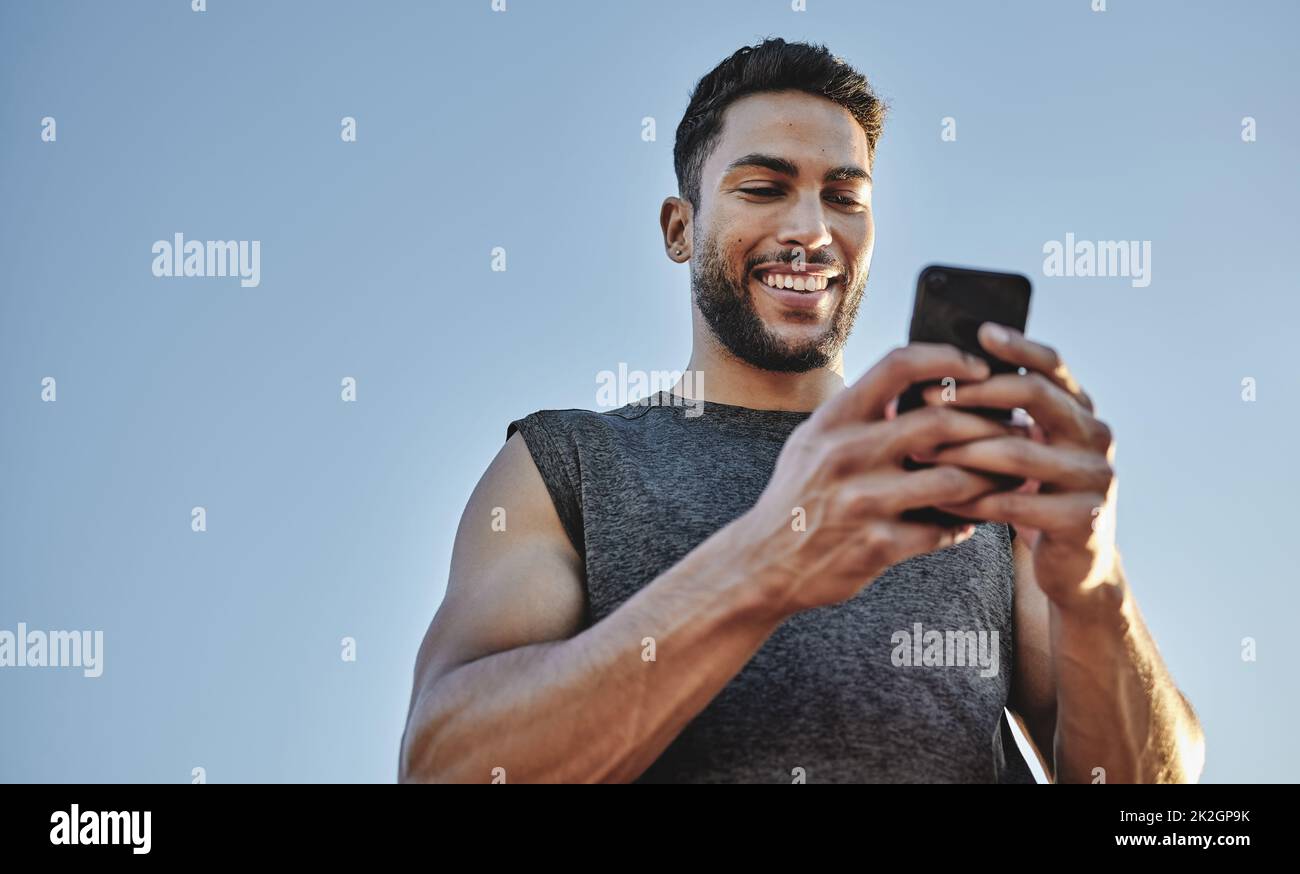 Building muscles with the help of modern tech. Low angle shot of a sporty young man using a cellphone while exercising outdoors. Stock Photo
