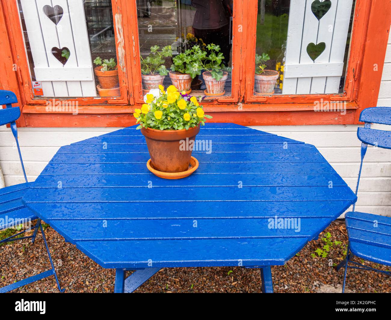 Angelsberg, Sweden - May 28, 2022: Blue table in front of the old cottage with white window shutter in the background Stock Photo