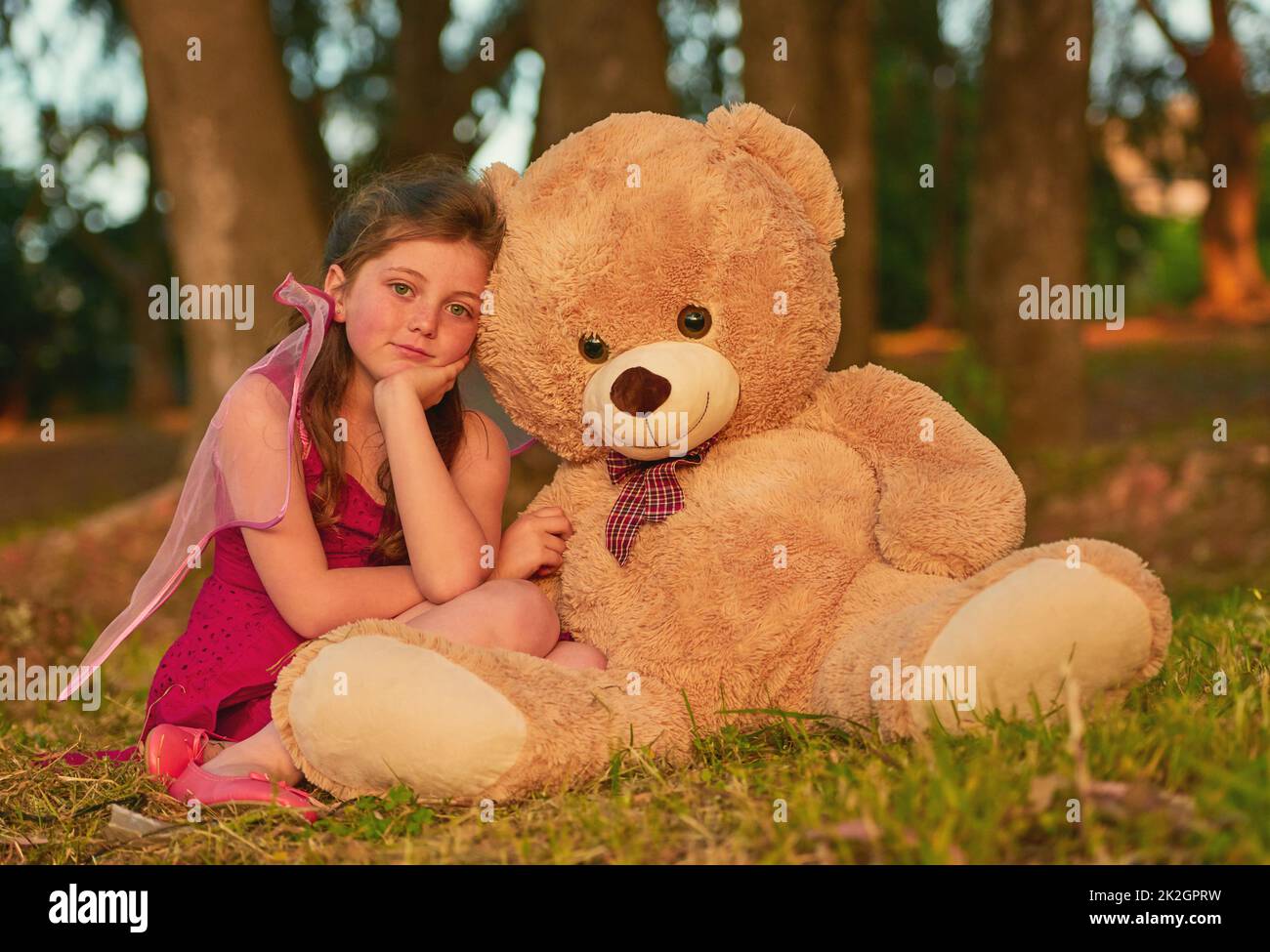 What more could a little girl want. Portrait of a cute little girl playing with a huge teddybear in the park. Stock Photo