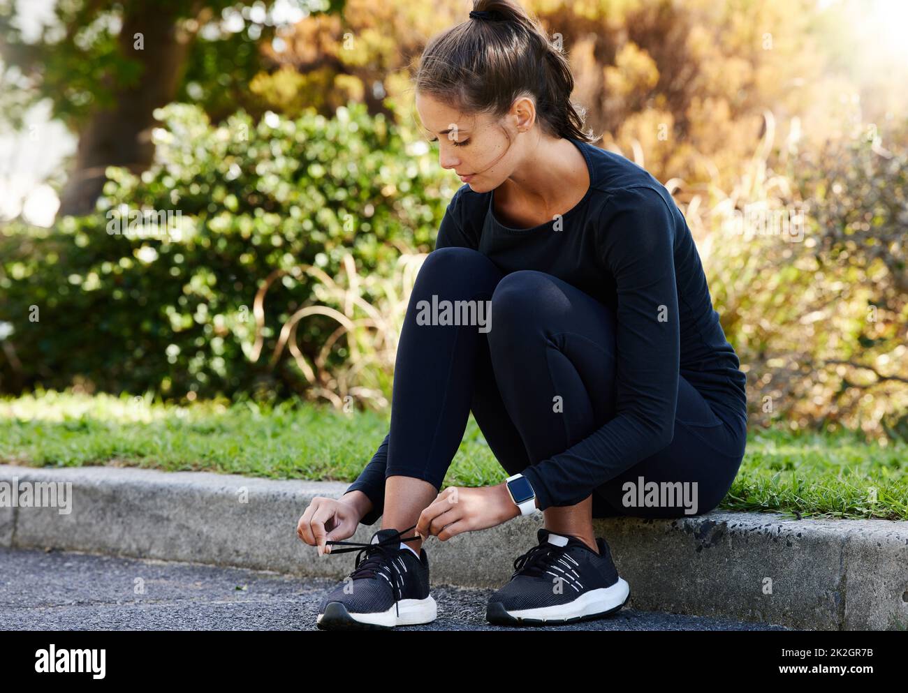 Making sure her laces are nice and tight. Full length shot of an attractive and athletic young woman tying her shoelaces while sitting on the curb outdoors. Stock Photo