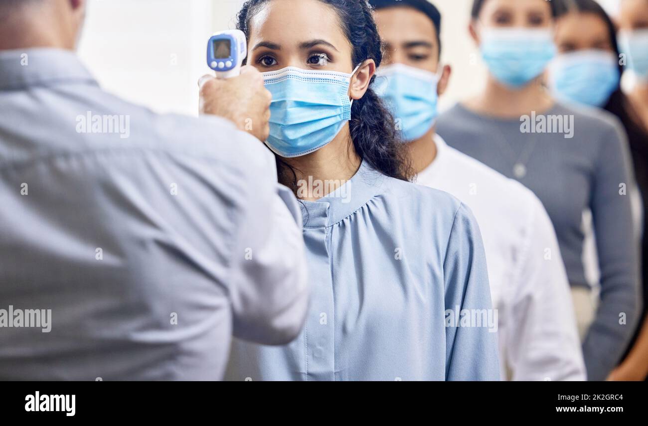 Complete your screening before heading into the office. Cropped shot of a group of businesspeople wearing masks lined up to be screened for covid 19. Stock Photo