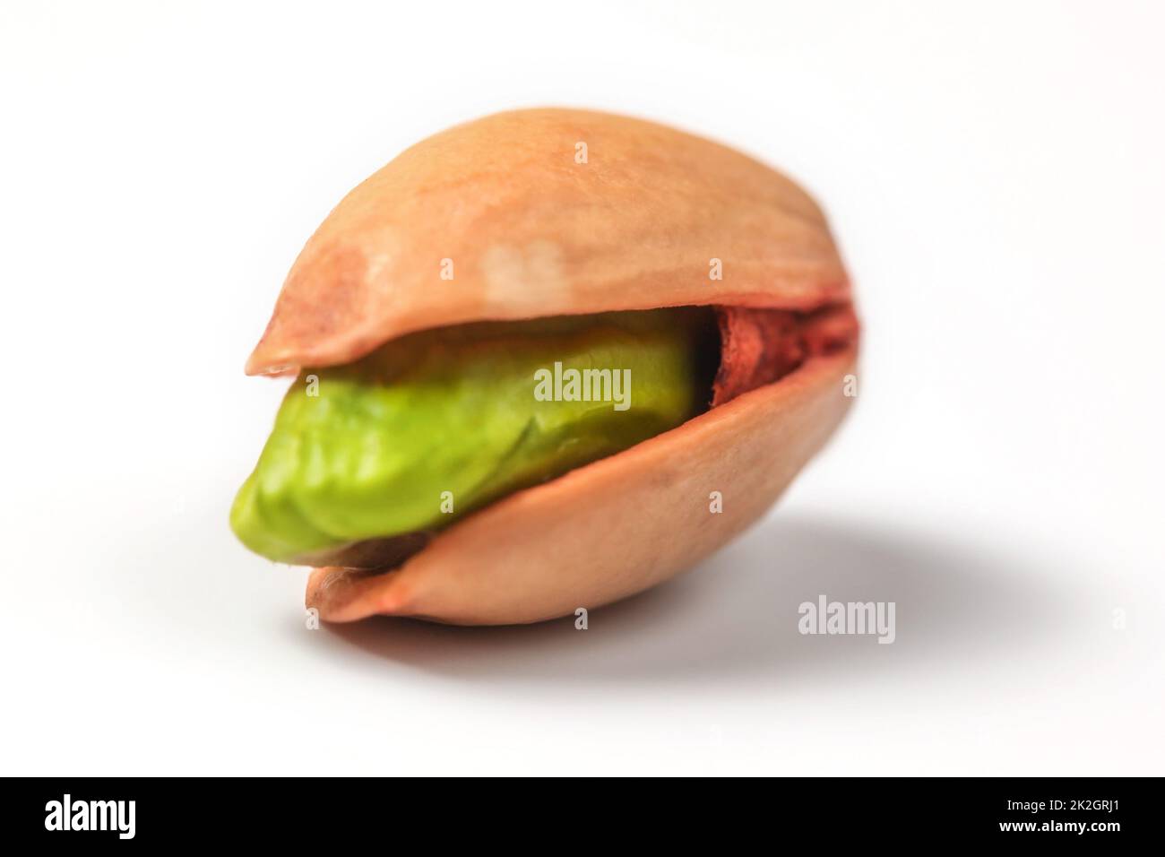 Single red Turkish pistachio, green nut visible under shell, isolated