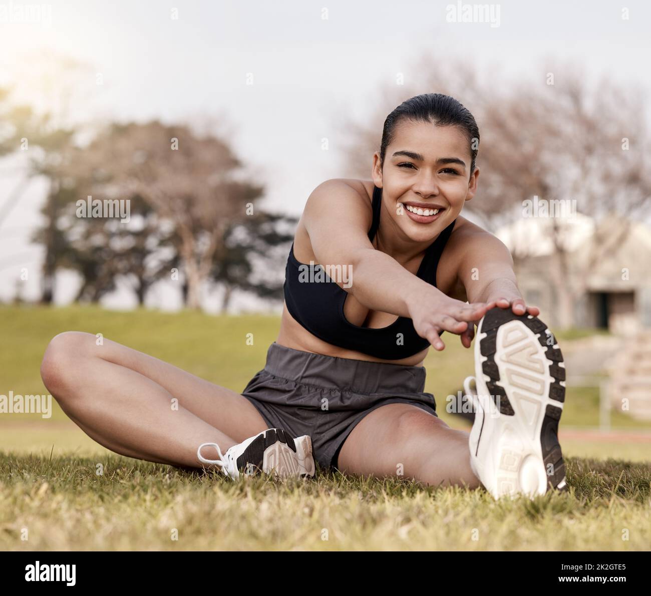 I always stretch before training. Full length shot of an attractive young woman sitting alone outside and stretching before playing sports. Stock Photo