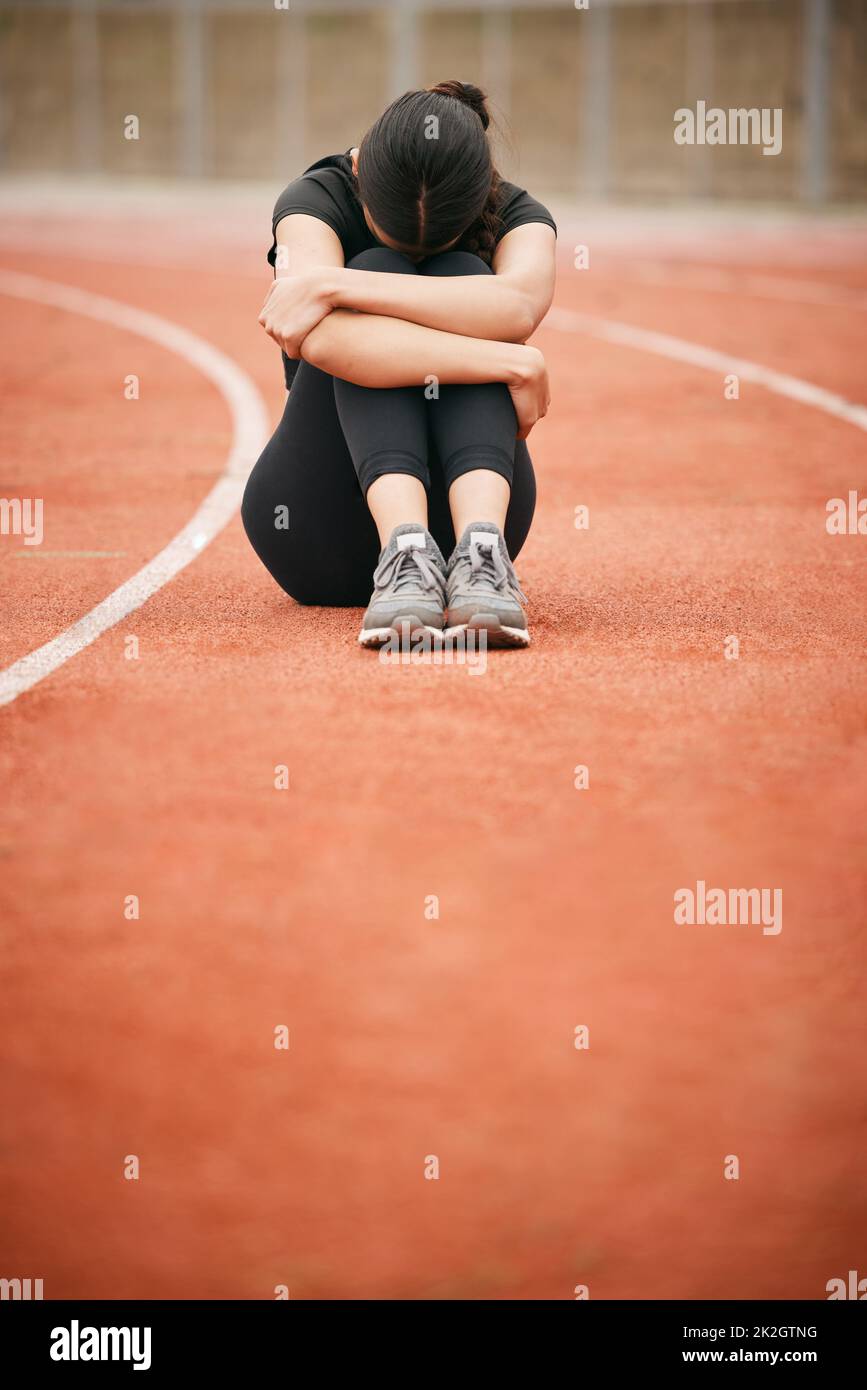 Today has been tough. Shot of a young woman looking upset while sitting on the track. Stock Photo