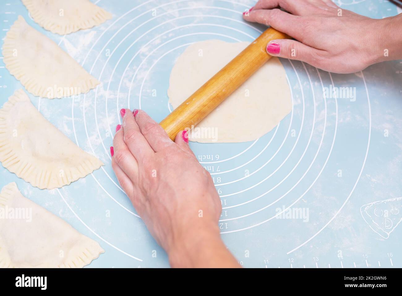 Test preparation. Female hands roll out the dough with a rolling pin on a silicone mat. Stock Photo