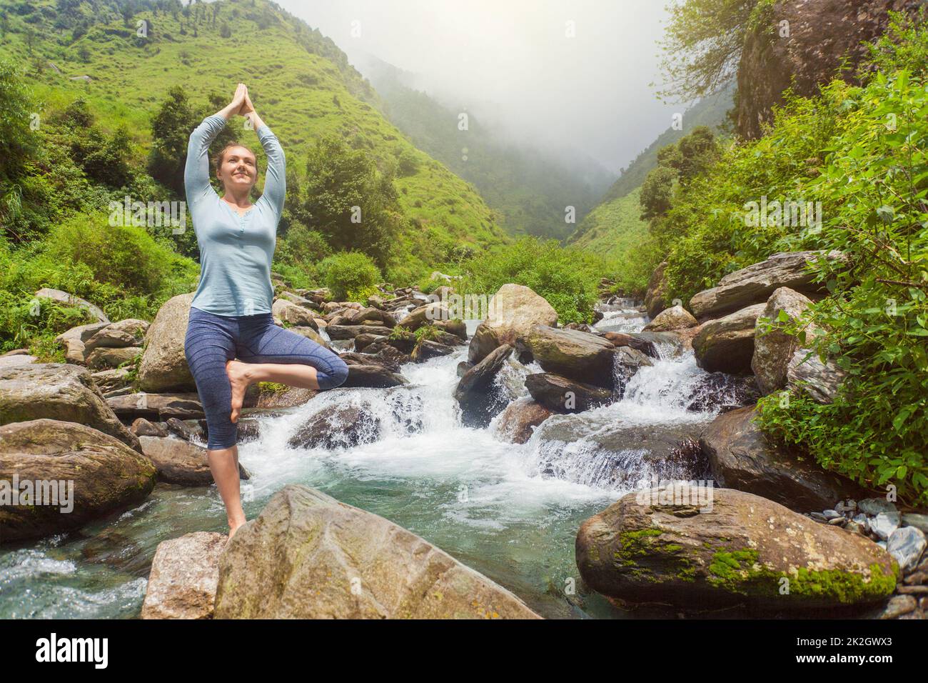 Woman in yoga asana Vrikshasana tree pose at waterfall outdoors Stock ...