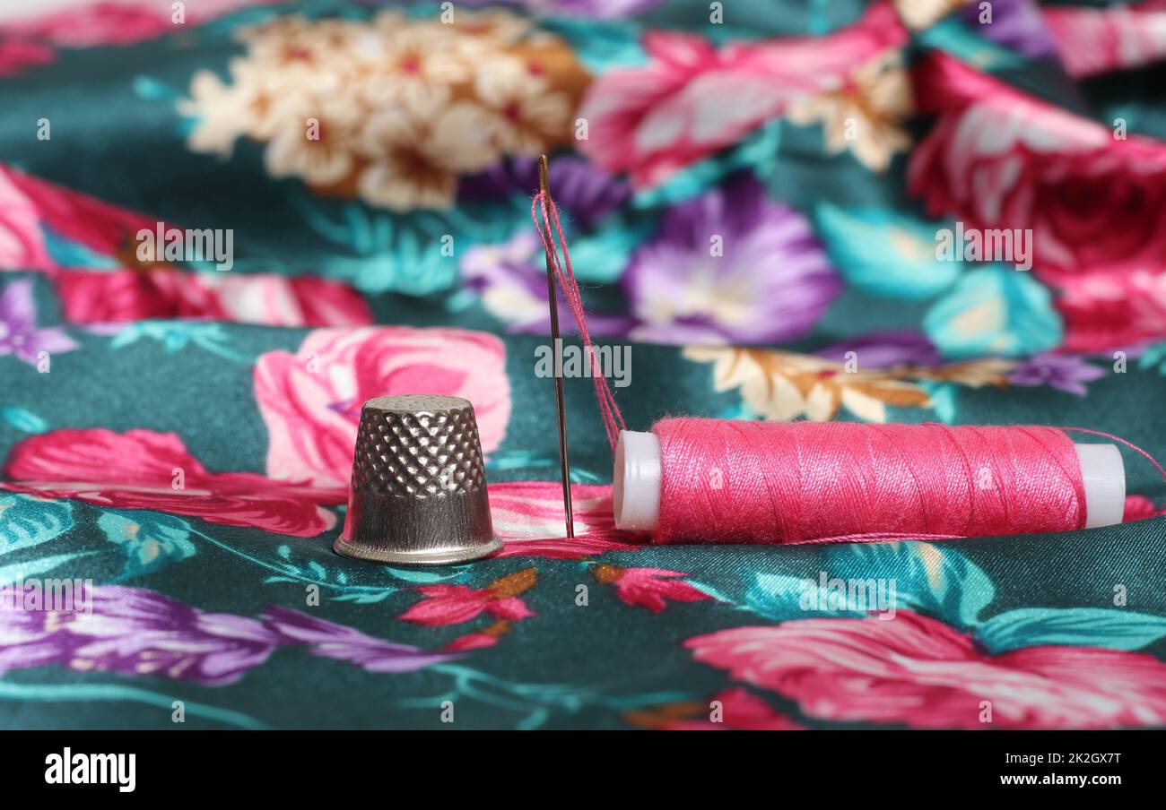 Thimble With Needle and Pink Thread on Vintage Floral Satin Fabric Stock Photo