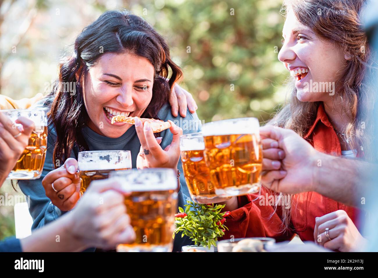 happy friends drinking beers and eating pizza outdoors and laughing together - focus on a young woman biting a slice of pizza - cheerful people, food Stock Photo