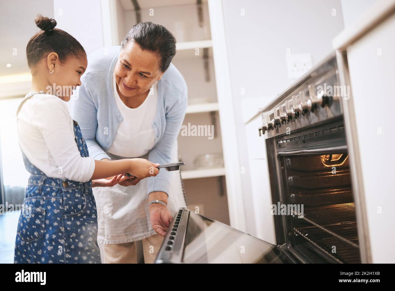 Dont get too close. Shot of a mature woman helping her grandchild safely open the oven at home. Stock Photo